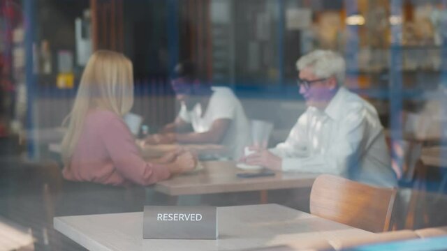 View through window of waiter setting RESERVED sign on restaurant table