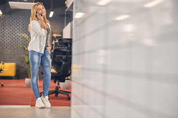 Cheerful young woman having phone conversation in office