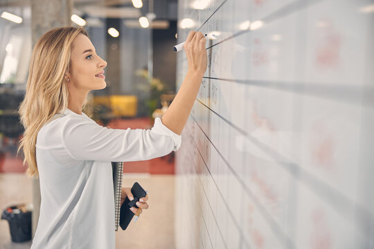 Attractive Young Woman Writing On Task Board In Office