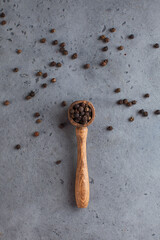 Black pepper peas in a wooden spoon on a gray background. Spices.
