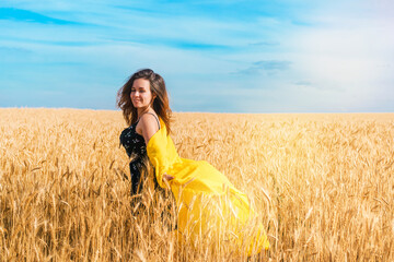Naklejka premium A young girl with long hair and a yellow robe fluttering in the wind is dancing in a wheat field