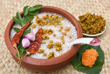Rice porridge, Kanji, gruel in clay pot palm mat background Kerala South India .congee, rice soup, green gram curry, chammanthi. Ayurveda diet  for immunity. Top view porridge Indian veg food.