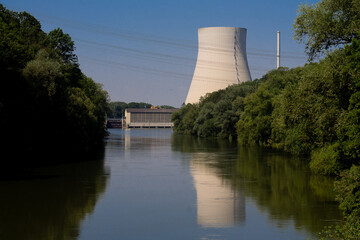 The cooling tower of a nuclear power plant is reflected in a river. In front of it is a hydropower...