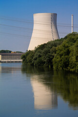 The cooling tower of a nuclear power plant is reflected in a river. In front of it is a hydropower...