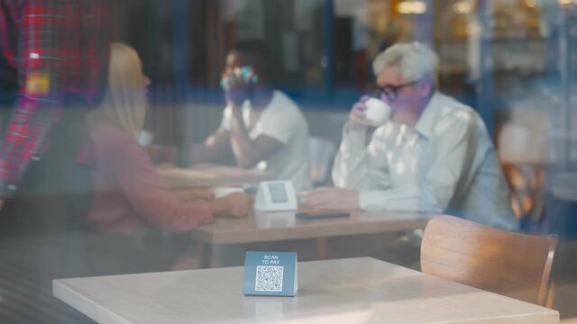View though window of waiter in apron setting sign with qr-code for scanning to pay on table