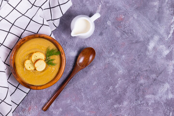 Lentil and pumpkin cream soup with dill and garlic in a wooden plate with a wooden spoon and buttercream