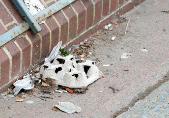 Small pile of garbage at the side of a sidewalk. Pile is next to a brick building. One of the pieces is the cardboard used to carry coffee cups. Room for text.