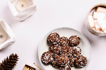 Swedish chocolate balls and cup of cocoa with marshmallow on grey concrete table. Cozy winter breakfast. Chokladbollar. Homemade healthy raw cocoa oatmeal balls sprinkled with coconut flakes