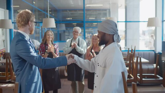 Side view of youmg male manager shaking hands and applauding to new african chef