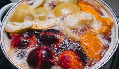 Fruit compote: apricots, plums, apples, cherries are cooked in a metal pan in boiled water with bubbles. Making juice on the stove.