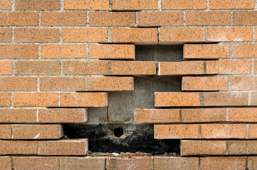 Bricks missing from a brick wall. Concrete blocks are behind the brick. 