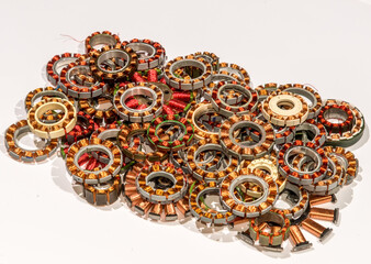 Coil assemblies from motors in hard drives and optical drives. The coils are in a pile to be recycled. They are wound with copper wire with red and clear enamel. View is from the top at an angle.
