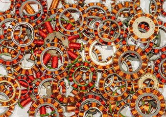 Coil assemblies from motors in hard drives and optical drives. The coils are in a pile to be recycled. They are wound with copper wire with red and clear enamel. Focus is near the middle.