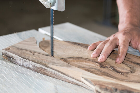 Carpenter hands working on band saw with wooden shape to create interior products.