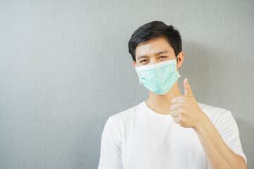close up asian man wear face mask with showing thumb up on grey background for coronavirus preventive design ads and banner concept
