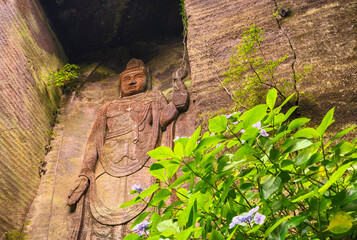Low angle view on the giant relief image of Japanese hyaku-shaku kannon buddha carved in Mount Nokogiri stone quarry and a purple hydrangeas flower.