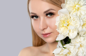 Obraz na płótnie Canvas Portrait of a beautiful blonde woman with long hair, beautiful fresh makeup and healthy clean skin with peonies in her hands. Makeup and cosmetology concept.