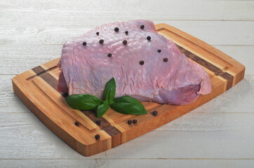 Fresh raw meat turkey thigh on a  wooden board, decorated with black pepper and green basil  leaves