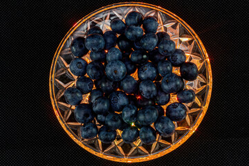 Still life of blueberries with yellow lighting on a black background.