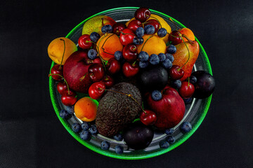 Still life of berries and fruit with green lighting on a black background.