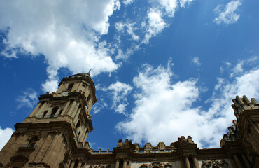 Obraz premium The beautiful cathedral of the historic city of Malaga. Angular view of the bell tower with ornate, decorative carvings. Blue sky and clouds - copy space.