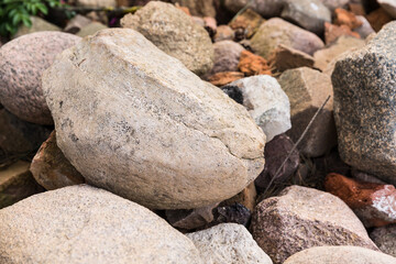 Natural stones with plants around. The texture of the stones of different sizes and colours on the grass. Stone background. 