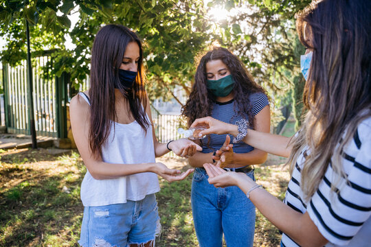 Young millennial women sanitize their hands with antibacterial gel in bottle disposable against the bacteria and virus of Coronavirus, Covid-19 in the park at sunset