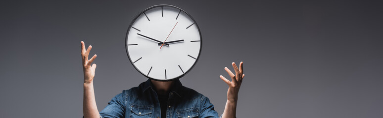 Horizontal image of man with clock on head gesturing on grey background, concept of time management