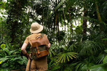 Woman botanist dressed in safari style in greenhouse, back view. Naturalist in khaki clothes,...