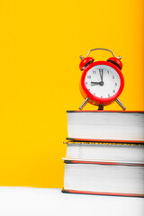 books and red clock on yellow background