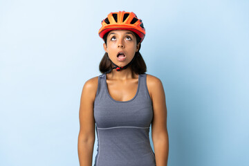 Young cyclist woman isolated on blue background looking up and with surprised expression
