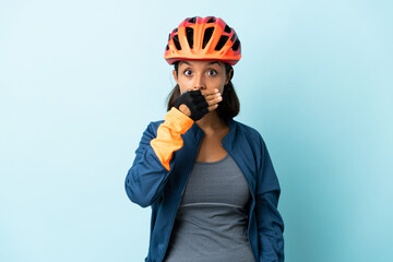 Young cyclist woman isolated on blue background covering mouth with hand