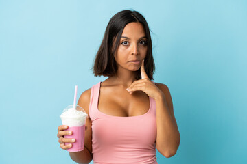 Young woman with strawberry milkshake isolated on blue background and thinking