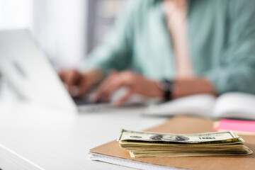 Selective focus of dollars on notebook and man using laptop at table, concept of earning online