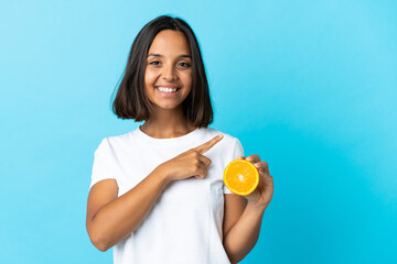 Young asian girl holding an orange isolated on blue background pointing to the side to present a product