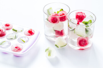 Cocktail glasses with berries in ice cubes on white table