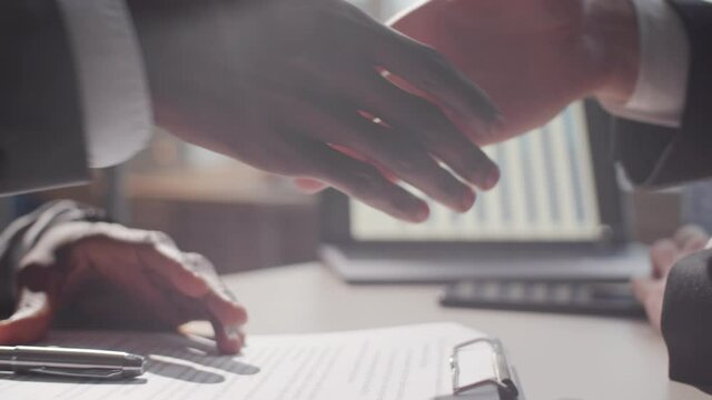Close up view of hands of black entrepreneur in formalwear signing agreement and then giving handshake to male business partner