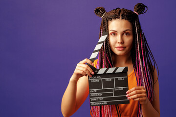 Young woman with braids holding clapper board close-up on purple background