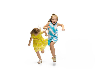 Happy children, little and emotional caucasian girls jumping and running isolated on white background. Looks happy, cheerful, sincere. Copyspace for ad. Childhood, education, happiness concept.