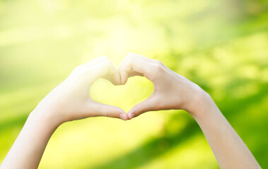 Child hands heart-shaped. Blurred background outdoors