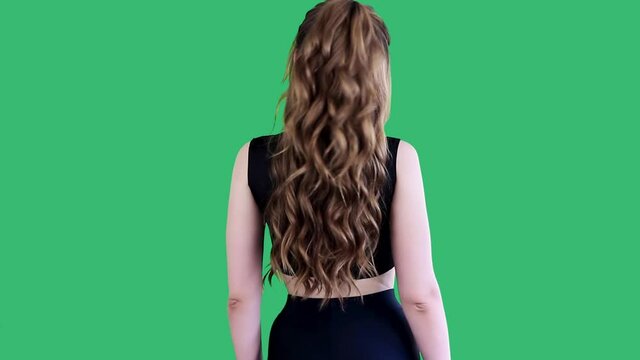 Back view of young long-haired girl doing dynamic stretching before physical activity,exercising lock behind the back.Isolated on green background.Healthy lifestyle,physical activity concept.