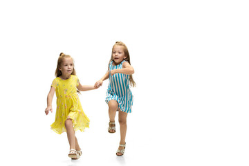 Happy children, little and emotional caucasian girls jumping and running isolated on white background. Looks happy, cheerful, sincere. Copyspace for ad. Childhood, education, happiness concept.