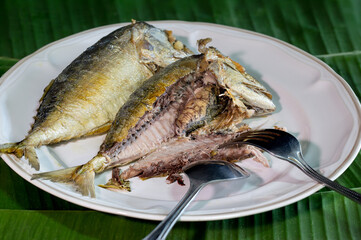 Rip fish fillets fried steamed mackerel ripe with fork and spoon, in white dish on green banana leaf