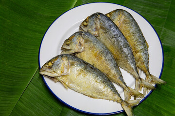 Fried steamed mackerel ripe, in white dish on green banana leaf