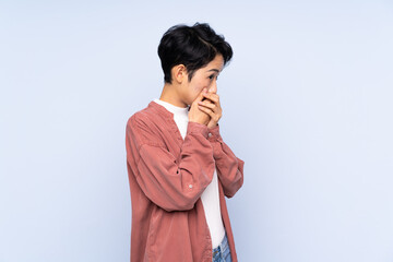 Young Asian girl over isolated blue background covering mouth and looking to the side