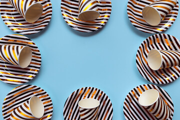 Golden, white and black striped paper glasses and dishes on blue  background. Creative party layout.