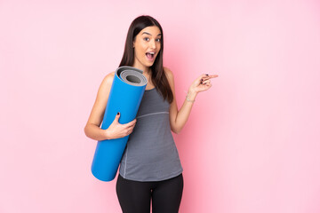 Young caucasian woman with mat isolated on pink background surprised and pointing finger to the side