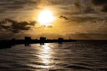 exciting backlight on the sea at the port of fiumicino; bright solar disc in a marine landscape with a yellow sky, shining sun on a swelling sea with silhouettes on the horizon; evening clouds 