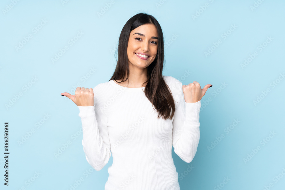 Wall mural Young caucasian woman isolated on blue background with thumbs up gesture and smiling