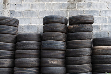The old tires were stacked beside the cement wall.Old car tires awaiting recycling.